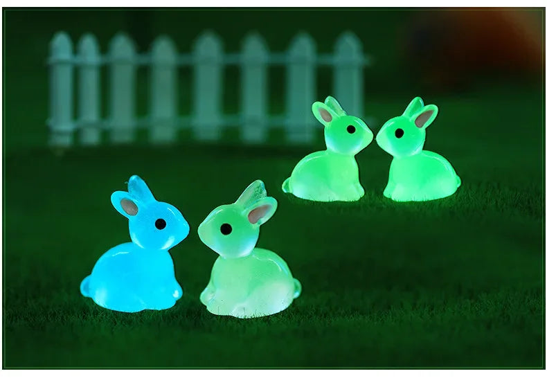 Two glowing green and blue resin bunny figurines resting on a dark green surface.