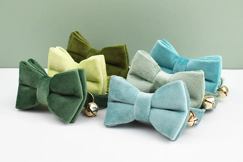 A collection of velvet cat collars in various shades of green and blue, featuring bow knots and gold safety buckles.