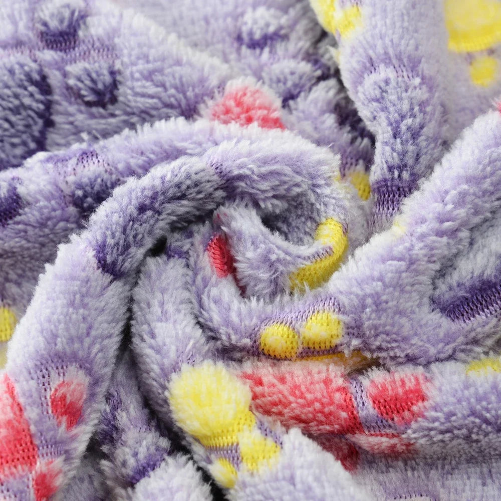 A close-up of a purple and gray fleece pet blanket with a paw print pattern, showing soft texture and folds.