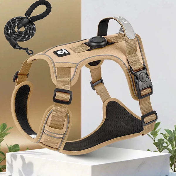 A tan dog harness with a black padded chest piece and a silver Airtag holder is displayed on a white surface.