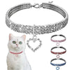 A silver rhinestone collar with a heart pendant displayed next to a white cat.