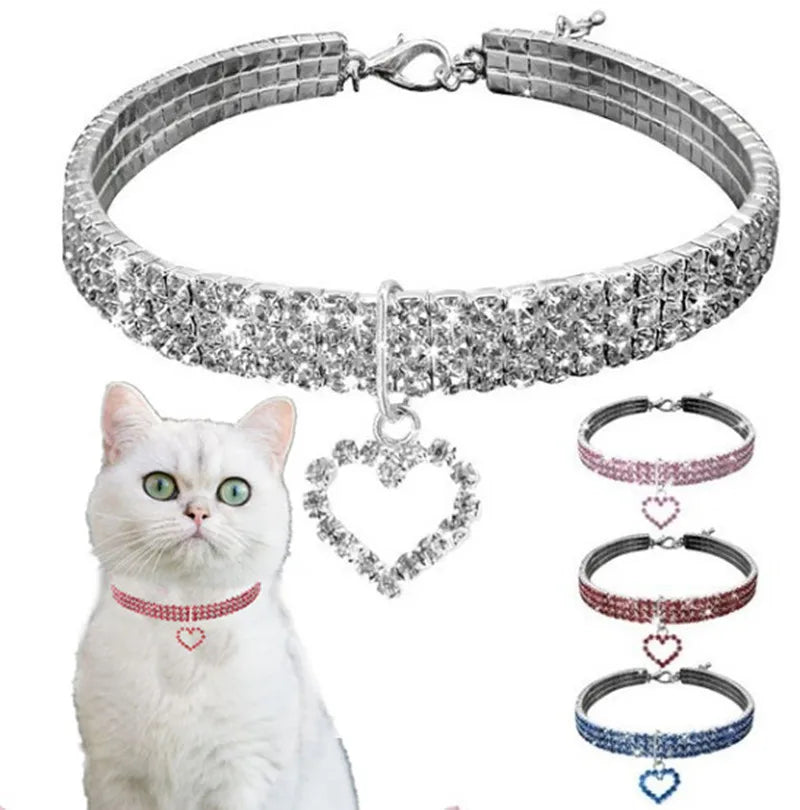 A silver rhinestone collar with a heart pendant displayed next to a white cat.
