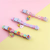 A colorful rainbow flower cat collar with a bell displayed on a light pink and yellow background.