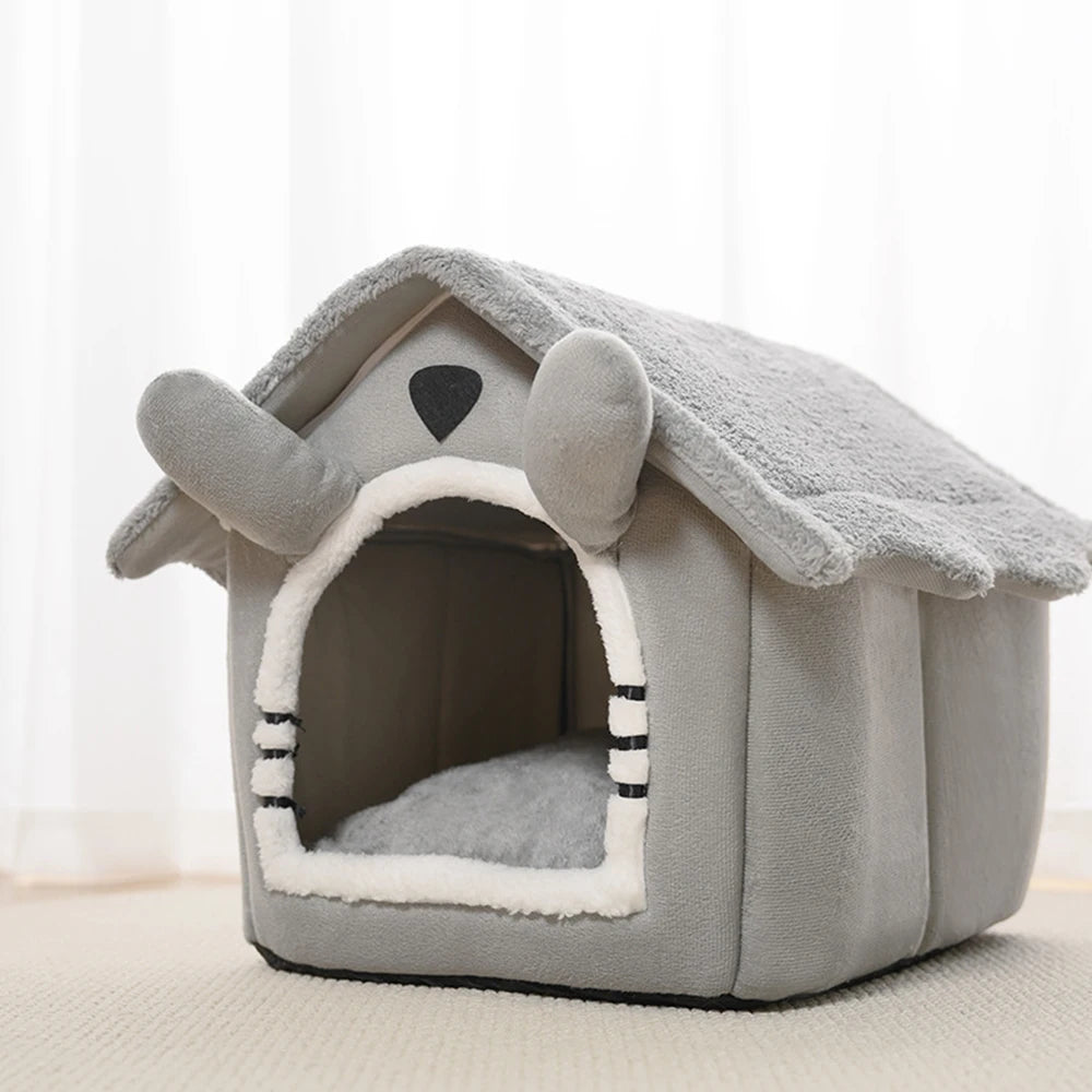 A gray fabric pet bed shaped like a house with an open mouth and floppy ears.