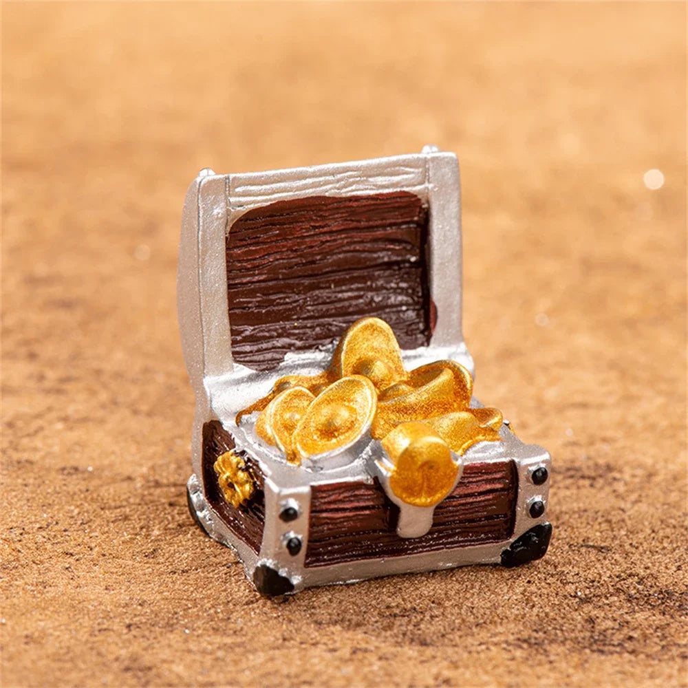 A miniature resin treasure chest with a lid open, revealing gold coins, resting on a brown textured surface.