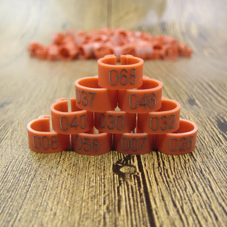 A stack of orange plastic bird identification foot rings with numbers on them resting on a wooden surface.