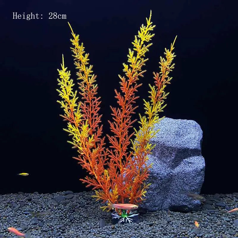 A tall, bushy artificial plant with orange and yellow foliage is displayed next to a gray rock on a dark gravel surface.