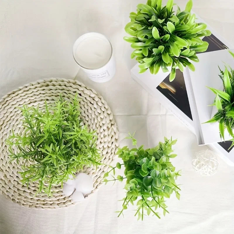 A collection of artificial bonsai potted plants displayed on a white surface with a woven mat and a white cup.