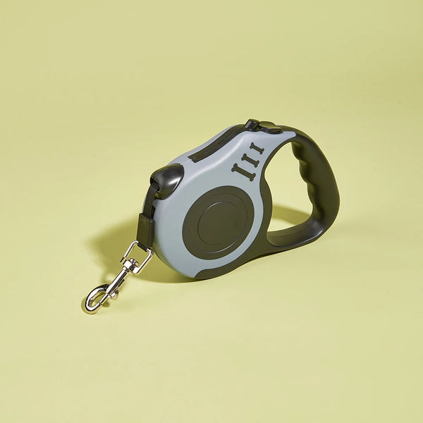 A gray automatic retractable dog leash with a dark green handle and silver clip, shown against a light yellow background.