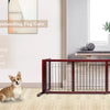 A brown wooden pet gate with vertical bars is shown in a bright room, next to a large mirror and a dog.