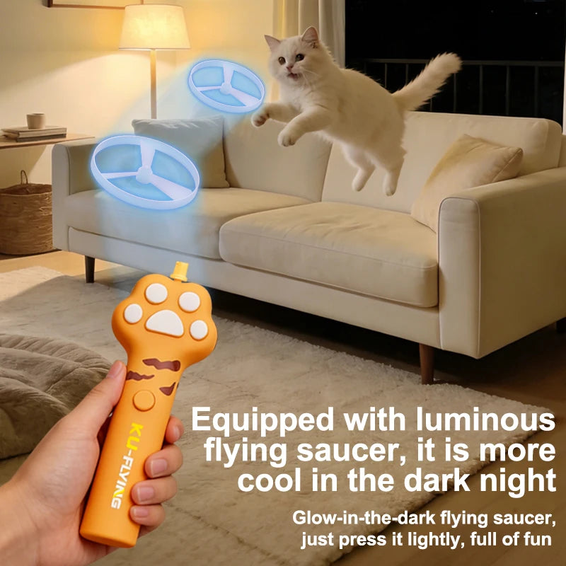 An orange interactive cat wand toy with a luminous flying saucer attachment is being held in a dimly lit living room.