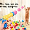 يد تمسك بقاذف أصفر به عشرين كرة صوف ملونة، وقطة مرئية في الخلفية.