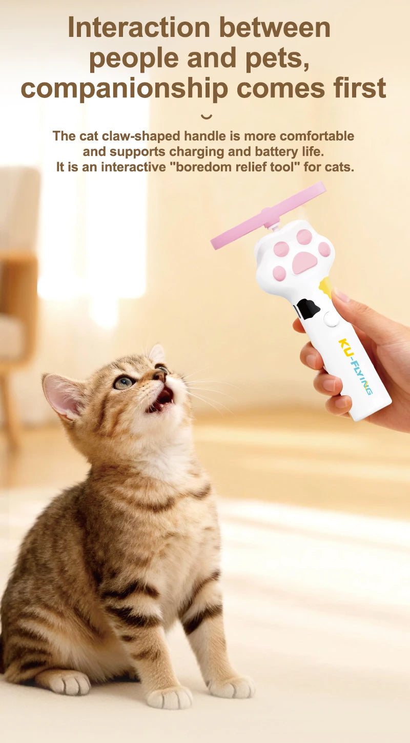 A hand holds a pink and white interactive cat wand toy with a flying saucer attachment, next to a tabby kitten.