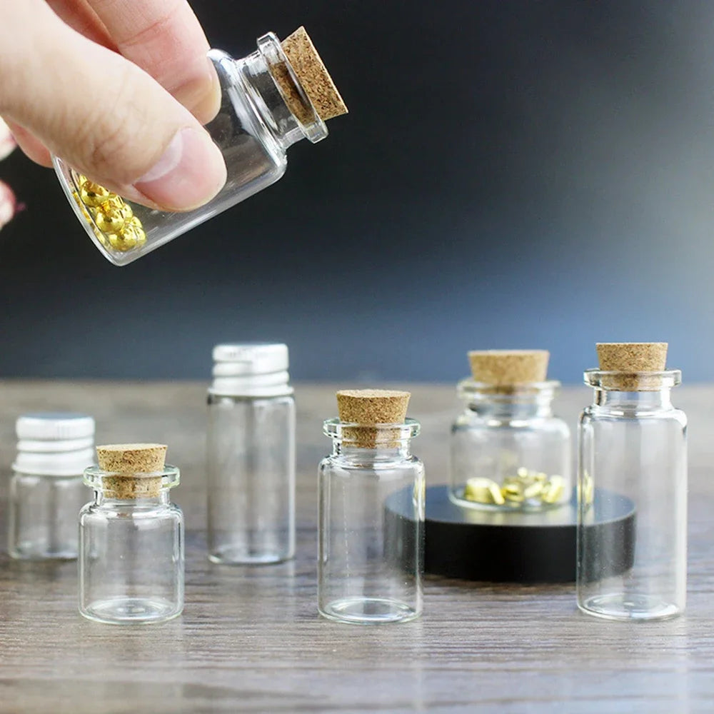 A hand holds a glass bottle filled with yellow powder, next to several empty mini glass bottles with cork stoppers.