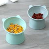 Two light blue pet feeding bowls, one filled with yellow kibble and the other with red kibble, sitting on a gray surface.