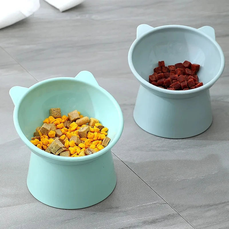 Two light blue pet feeding bowls, one filled with yellow kibble and the other with red kibble, sitting on a gray surface.