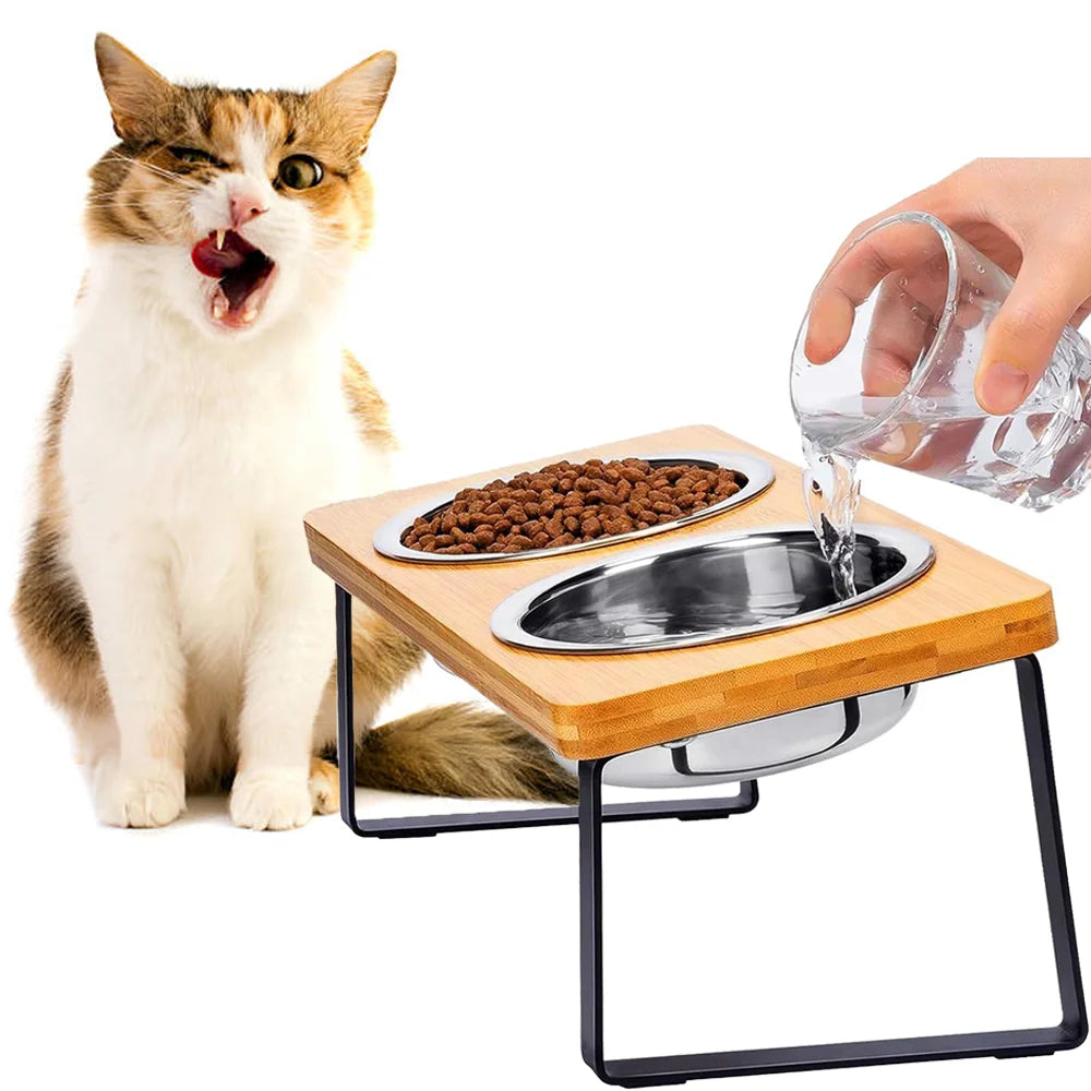 A cat looks at a wooden feeding stand holding stainless steel bowls for pet food.