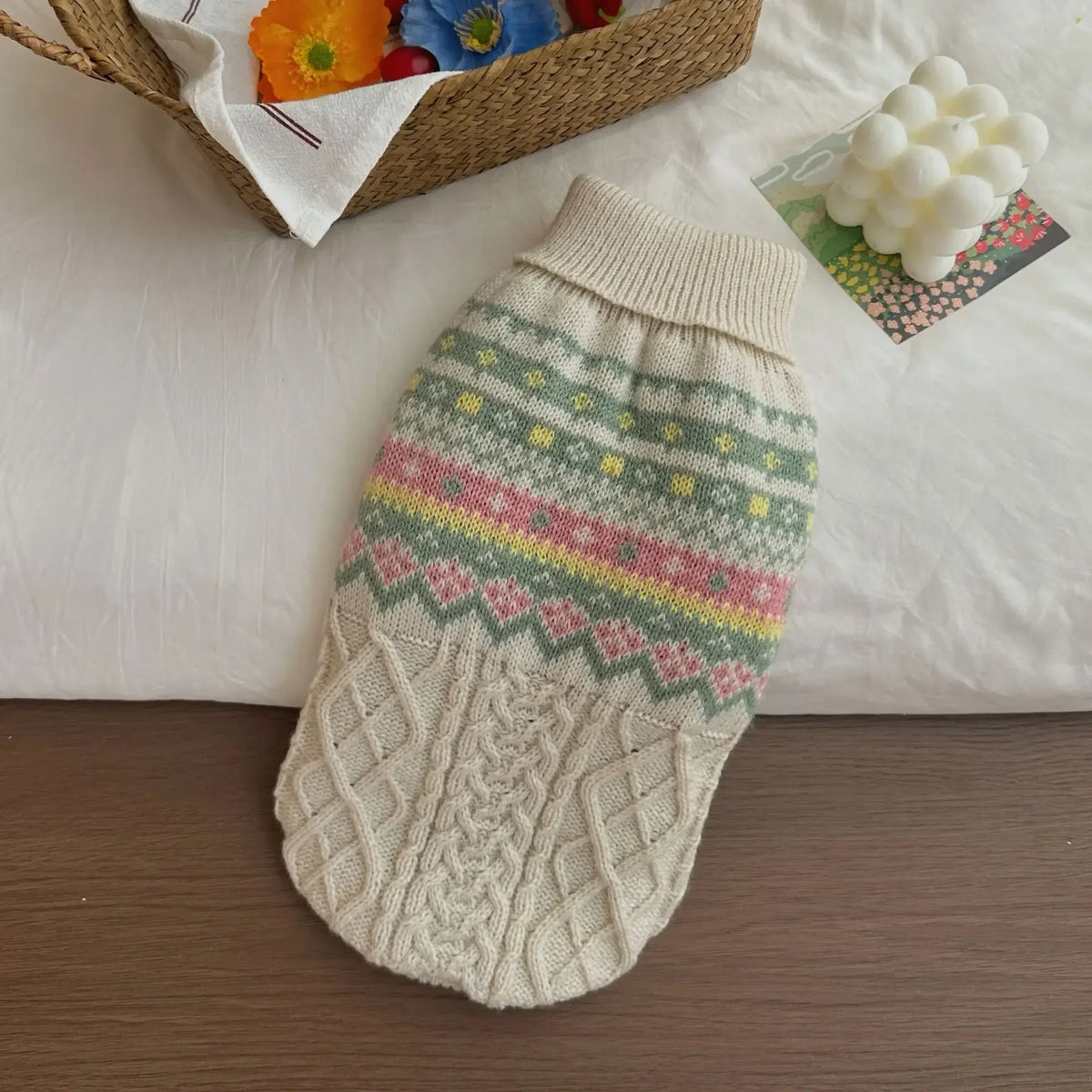 A knitted pet sweater for dogs and cats featuring multicolored stripes and a cream-colored cuff, resting on white fabric.