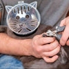 A person is holding a clear, cat-shaped grooming hood for pets with pliers.