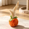 An orange plush ball topped with a feathery streamer, displayed on a light surface.