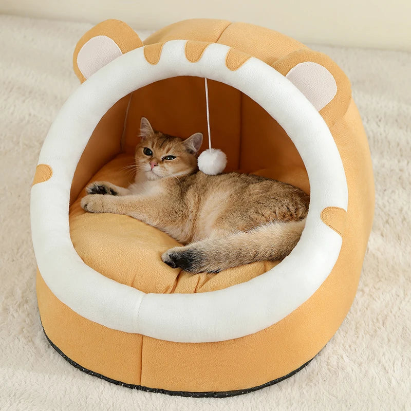 A fluffy ginger cat is relaxing inside a round, orange and white cat-shaped bed.