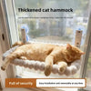 A fluffy orange cat relaxing in a thick, white cat hammock suspended in a window with suction cups.