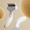A white one-key press detangling pet grooming brush is shown against a background of light brown pet hair.