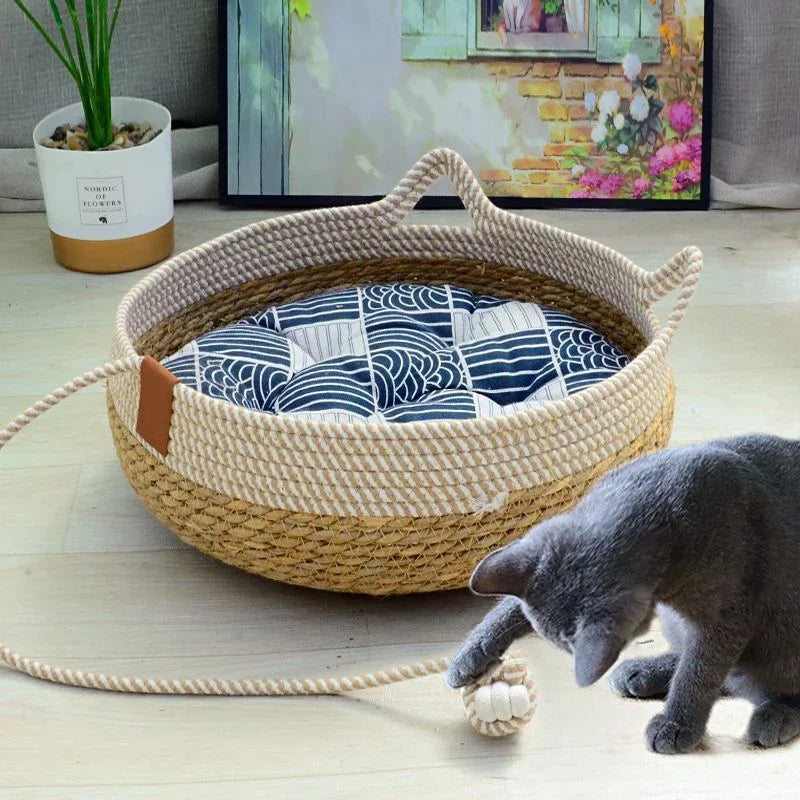 A woven rattan cat bed with a removable cushion is shown on a light wooden floor.