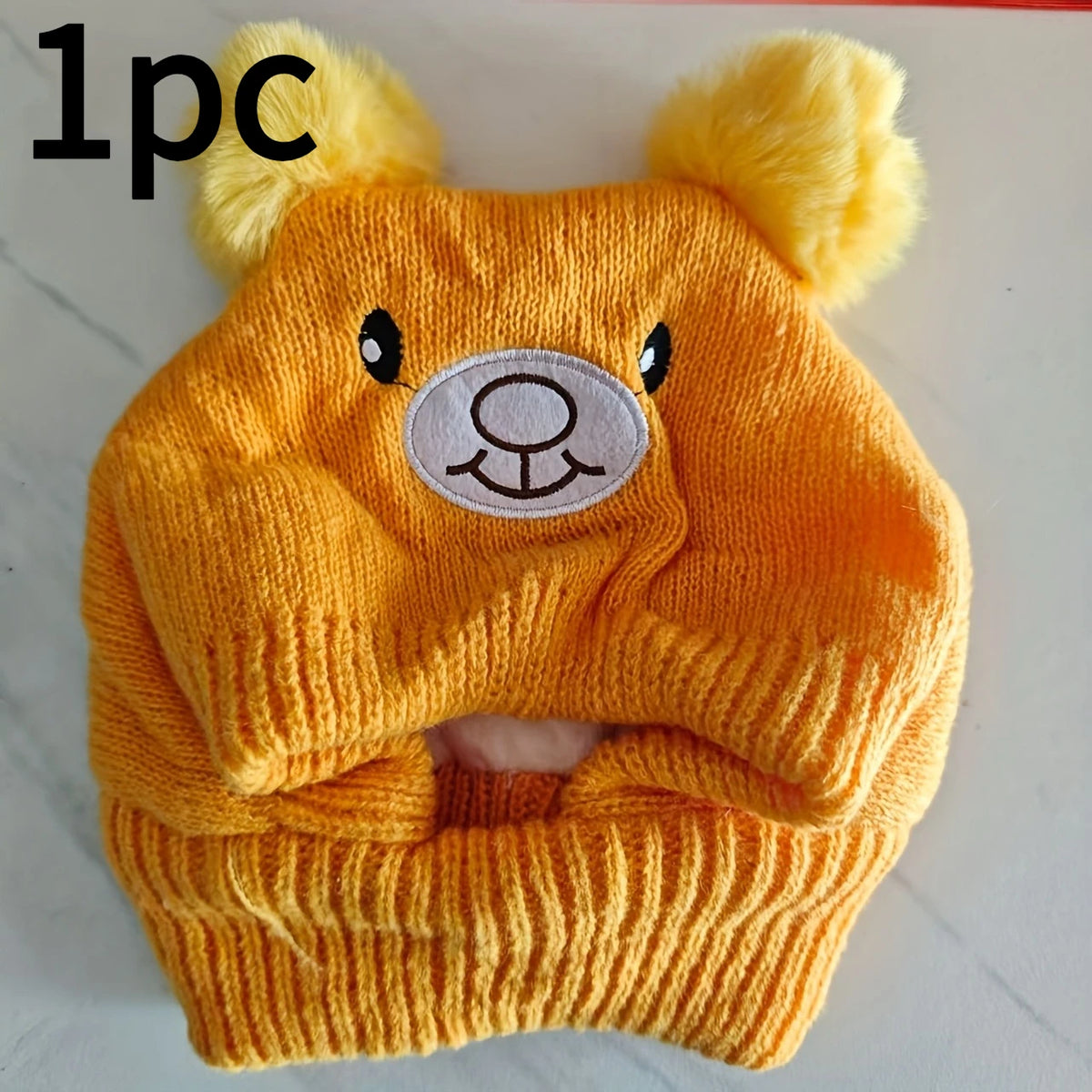A knitted orange dog ear hat featuring bear ears and a circular embroidered face design.