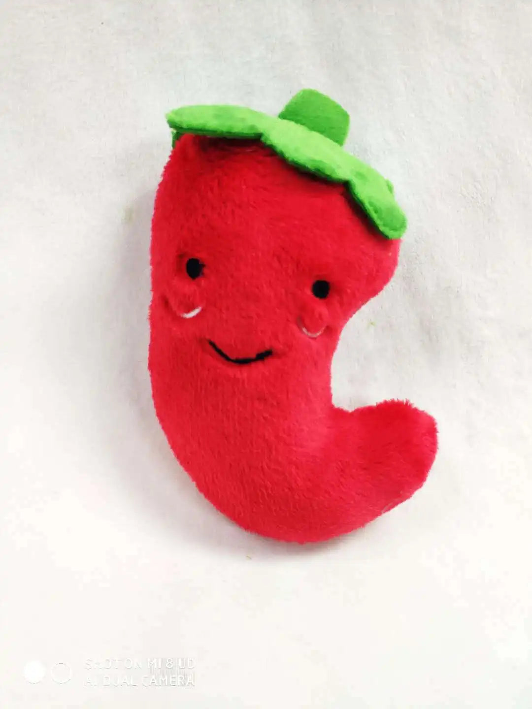 A bright red, bone-shaped squeaky plush dog toy with green leaves on top.