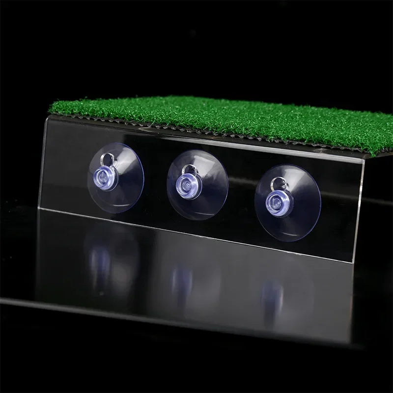 A black platform with three suction cups is placed on a green textured surface.