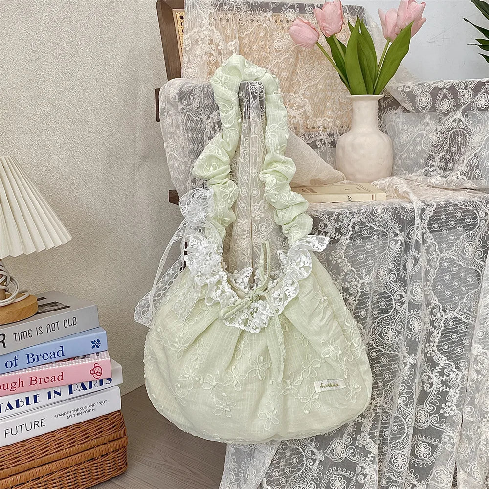 A pale green floral lace bowknot shoulder bag with a pleated design displayed on a white lace tablecloth.