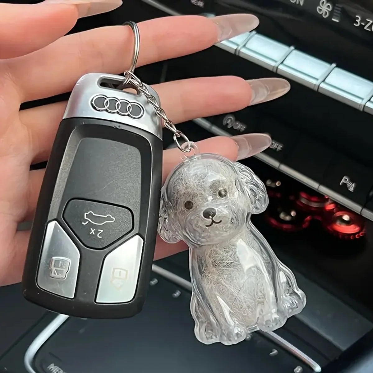 A silver pet hair storage keychain featuring a dog design, held by a hand against an electronic device.