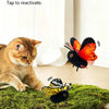 A small orange and black butterfly toy is shown flying near a tabby cat on a green surface.