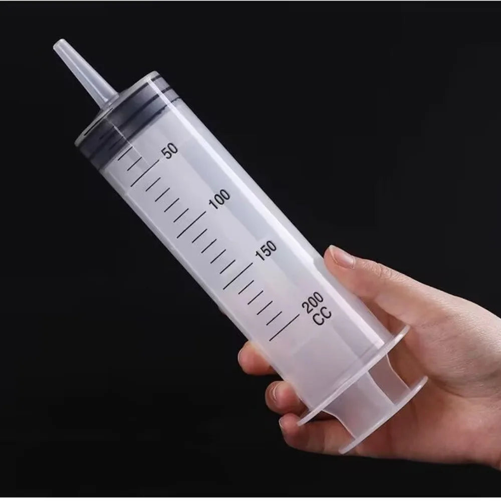 Eine Hand hält eine klare Plastikspritze mit Volumenangaben, die das Werkzeug zur Ölförderung demonstriert.