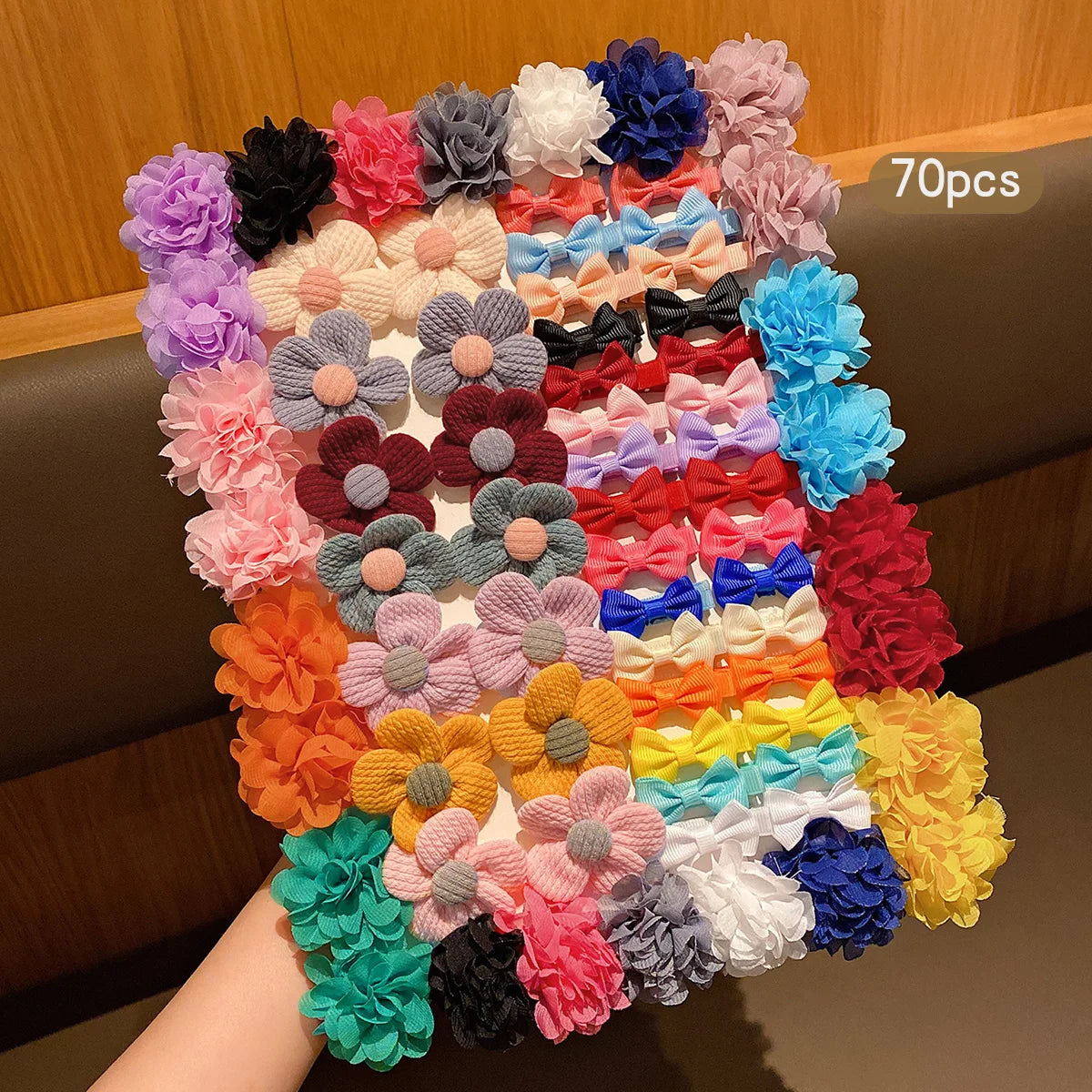 A large assortment of 70 fabric hair clips in various colors and floral patterns displayed on a wooden surface.