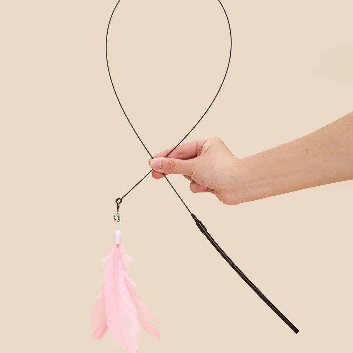A hand holds a black feather wand toy with a suction cup and pink feathers against a beige background.