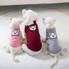 Three small white dogs wearing knitted winter pet sweaters in pink, maroon, and gray.