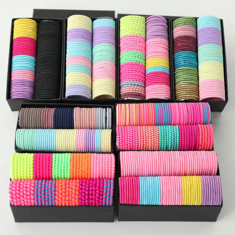 Colección de bandas elásticas de cabello coloridas en varios tonos y texturas, presentadas en empaque negro.