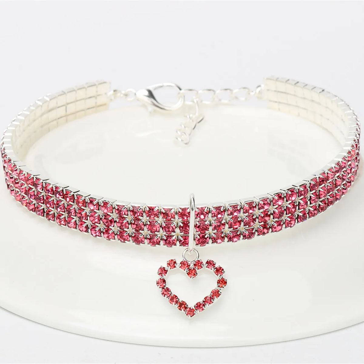 A silver-toned collar with a pink rhinestone band and a heart pendant displayed on a white plate.