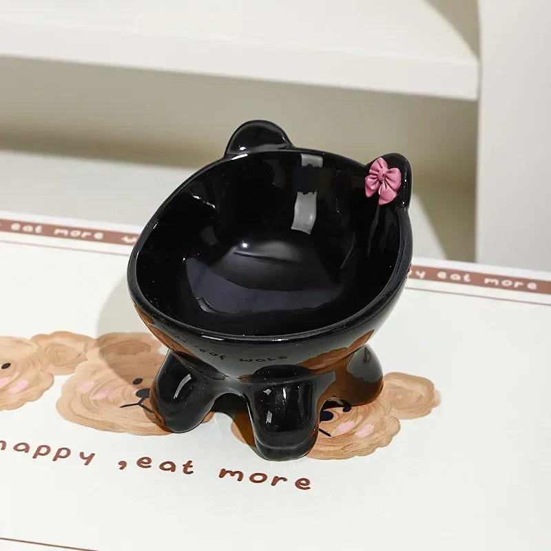 A black ceramic cat food bowl with a raised, tilted design sits on a white surface.