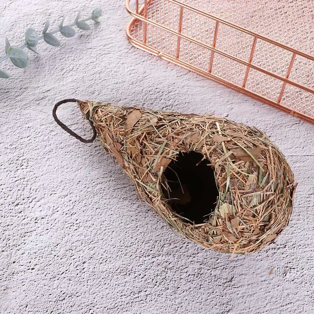 A hand-woven grass bird nest decoration with a dark entrance, resting on a light surface next to a copper wire basket.