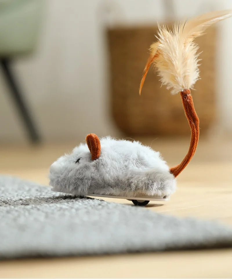 A small, fluffy gray mouse cat toy with an orange tail is resting on a gray fabric surface.