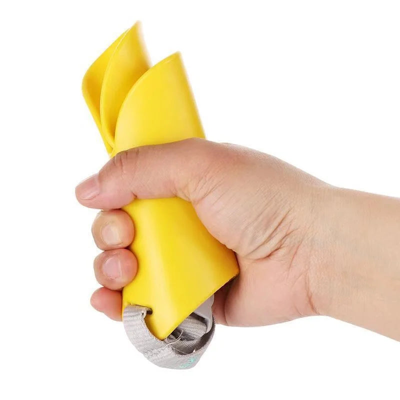 A hand is holding a yellow soft silicone dog muzzle with an adjustable fit and a metal clip.