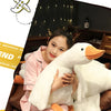 A woman is cuddling a white plush goose body pillow in a brown armchair.