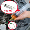 Eine Hand hält eine Plastikspritze mit einer klaren Flüssigkeit, zur Ölextraktion aus einem Motorbauteil.