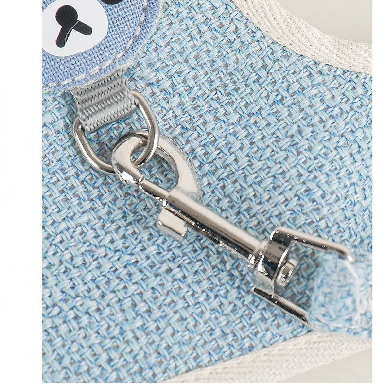 A close-up of an adjustable nylon dog harness and leash set with silver hardware on a light blue patterned fabric.