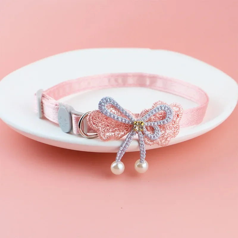 Pink lace bow cat collar with a silver bead charm and dangling pearl bells displayed on a white plate.