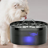 A white cat is looking at a black automatic cat water fountain with blue light glowing underneath.