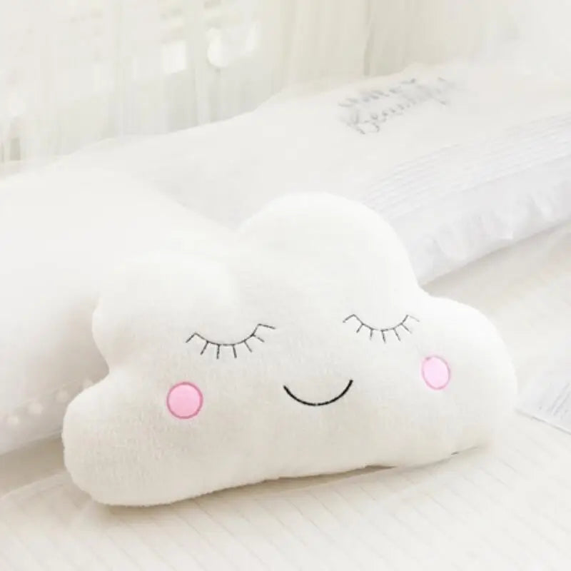 A white cloud shaped plush pillow with closed eyes and a smiling expression resting on a white surface.